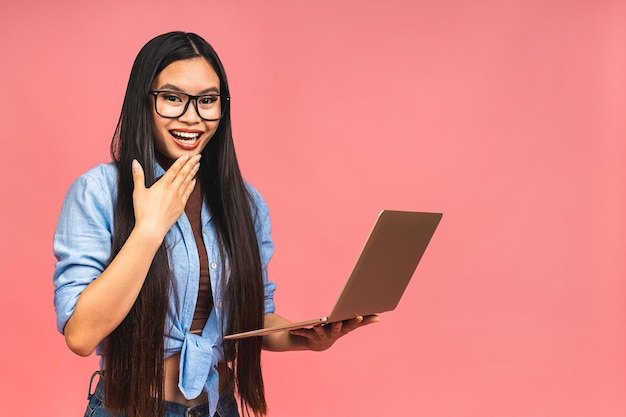 Retrato de una mujer de negocios asiática feliz trabajando en una laptop aislada de fondo rosa