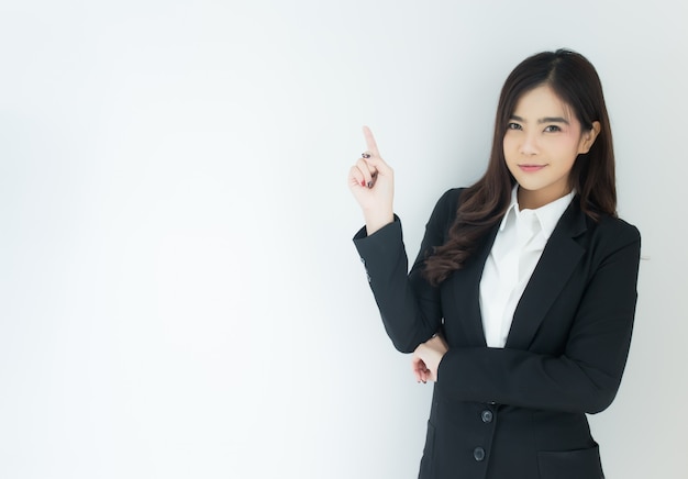 Retrato de la mujer de negocios asiática joven que señala para arriba sobre el fondo blanco.