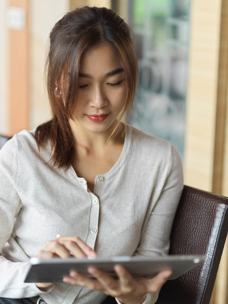 Retrato de mujer de negocios asiática que se concentra y trabaja en la tableta mientras sostiene el lápiz óptico