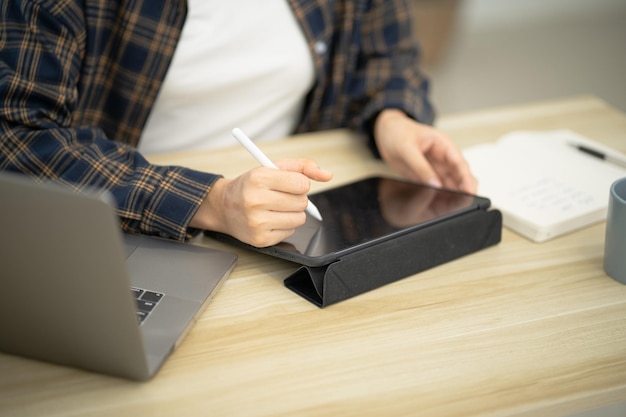 Retrato de una mujer de negocios asiática que trabaja desde la oficina leyendo y escribiendo notas en un bloc de notas trabajando en una computadora portátil en su estación de trabajo