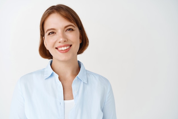 Retrato de mujer de negocios en blusa azul, sonriendo con dientes blancos, con aspecto de profesional. Trabajadora emprendedora de pie contra la pared blanca