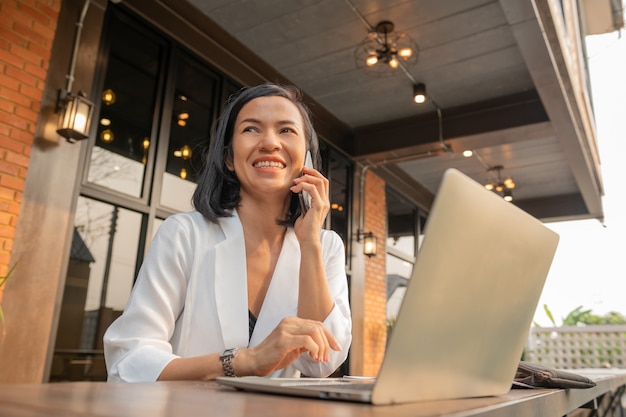 Retrato de mujer de negocios en un café usando una computadora portátil y hablando por un teléfono móvil