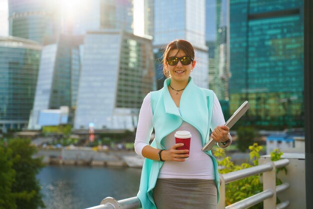 Retrato de mujer de negocios caminando y sonriendo al aire libre con laptop y taza de café