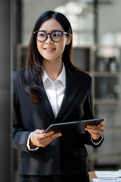 Retrato de una mujer de negocios elegante e influyente con gafas en traje formal sosteniendo una tableta de pie en el cargo