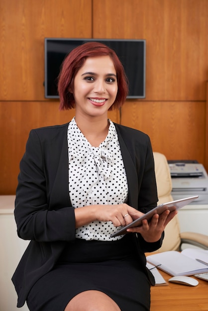 Retrato de mujer de negocios elegante sonriente sentada en el escritorio de oficina y usando la aplicación para organizar y planificar