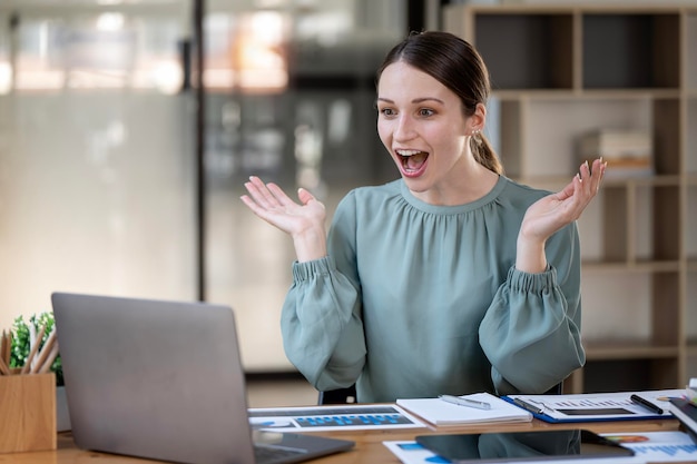 Retrato de una mujer de negocios emocionada mirando una laptop con satisfacción sentada en su oficina