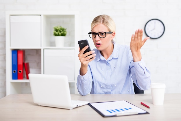 Retrato de mujer de negocios enojada con teléfonos inteligentes en la oficina