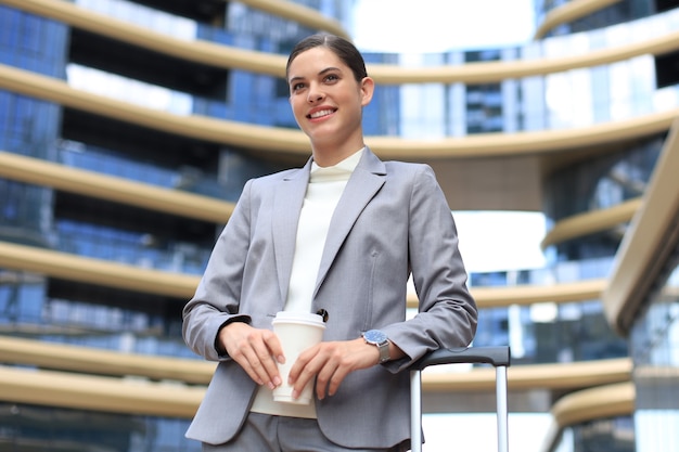 Retrato de mujer de negocios exitosa que va a trabajar con café caminando cerca del edificio de oficinas en la calle de la ciudad.