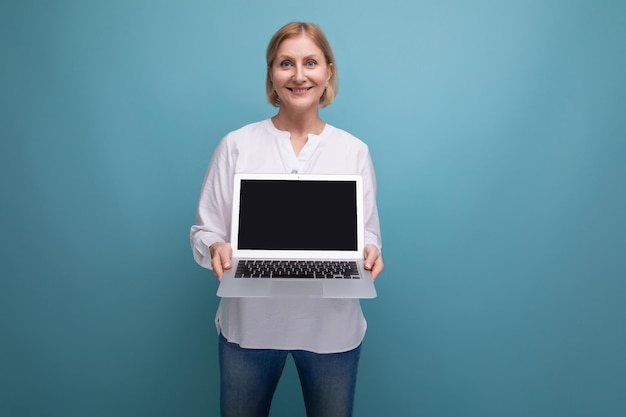 Retrato de mujer de negocios feliz de mediana edad con cabello rubio usando laptop con mocup