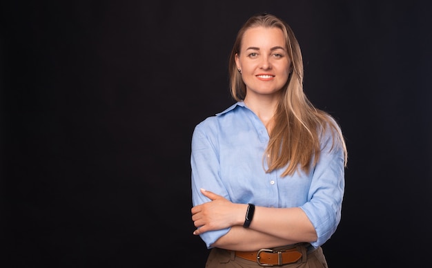 Retrato de mujer de negocios hermosa de pie con los brazos cruzados sobre fondo oscuro y mirando a la cámara