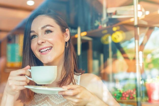 Retrato de mujer de negocios joven feliz con taza en las manos tomando café en el restaurante