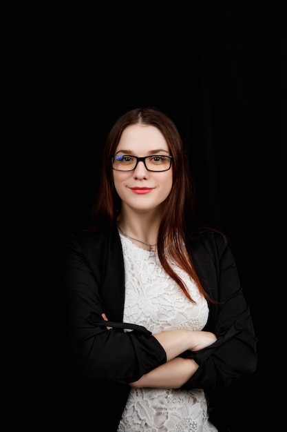 Retrato de mujer de negocios joven con gafas en una chaqueta negra sobre negro.