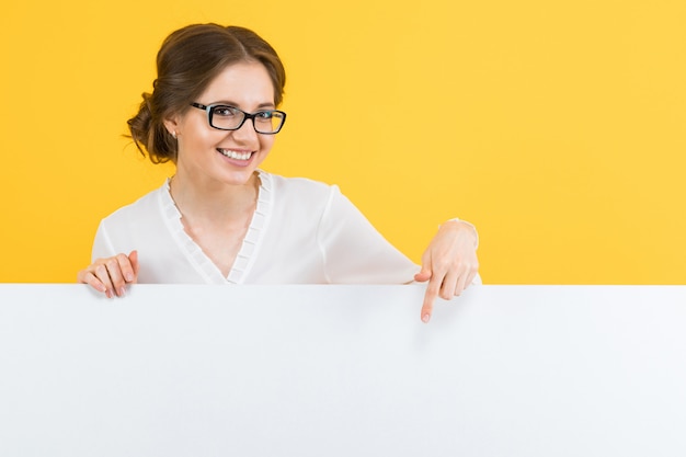 Retrato de mujer de negocios joven hermosa confidente que muestra la cartelera en blanco sobre fondo amarillo