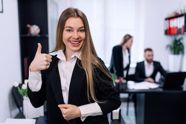 Retrato de mujer de negocios joven en el interior de la oficina de inicio moderno mostrando los pulgares para arriba