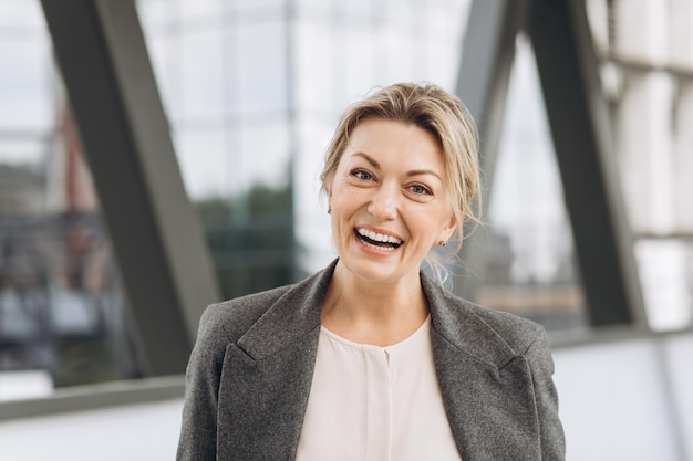 Retrato de una mujer de negocios madura sonriendo con emociones en el moderno fondo urbano y de edificios de oficinas