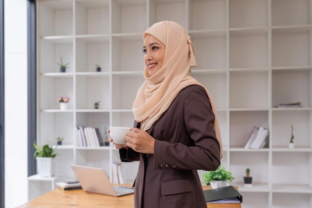 Foto retrato de una mujer de negocios musulmana con hijab segura sosteniendo una taza de café en el lugar de trabajo