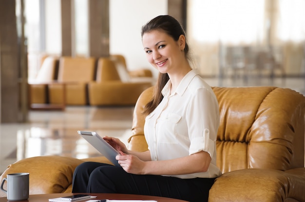 Retrato de mujer de negocios ocupada trabajando en ipad mientras está sentado en el sofá. Pequeños negocios.