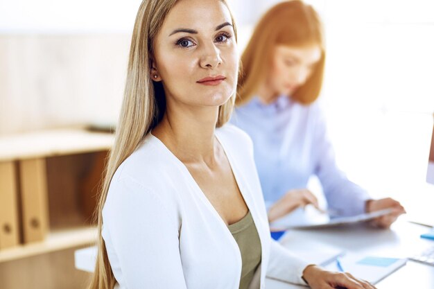 Retrato de mujer de negocios en la oficina soleada. Empresarios o colegas discutiendo algo en la reunión mientras están sentados en el escritorio de la oficina. Estilo de ropa informal. Concepto de auditoría, impuestos o abogado.