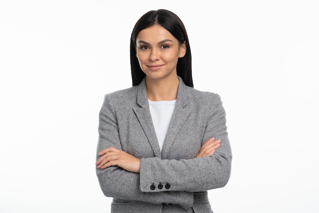 Retrato de mujer de negocios positiva de pie con los brazos cruzados, mirada amable y sonrisa encantadora. Tiro de estudio interior aislado sobre fondo blanco.