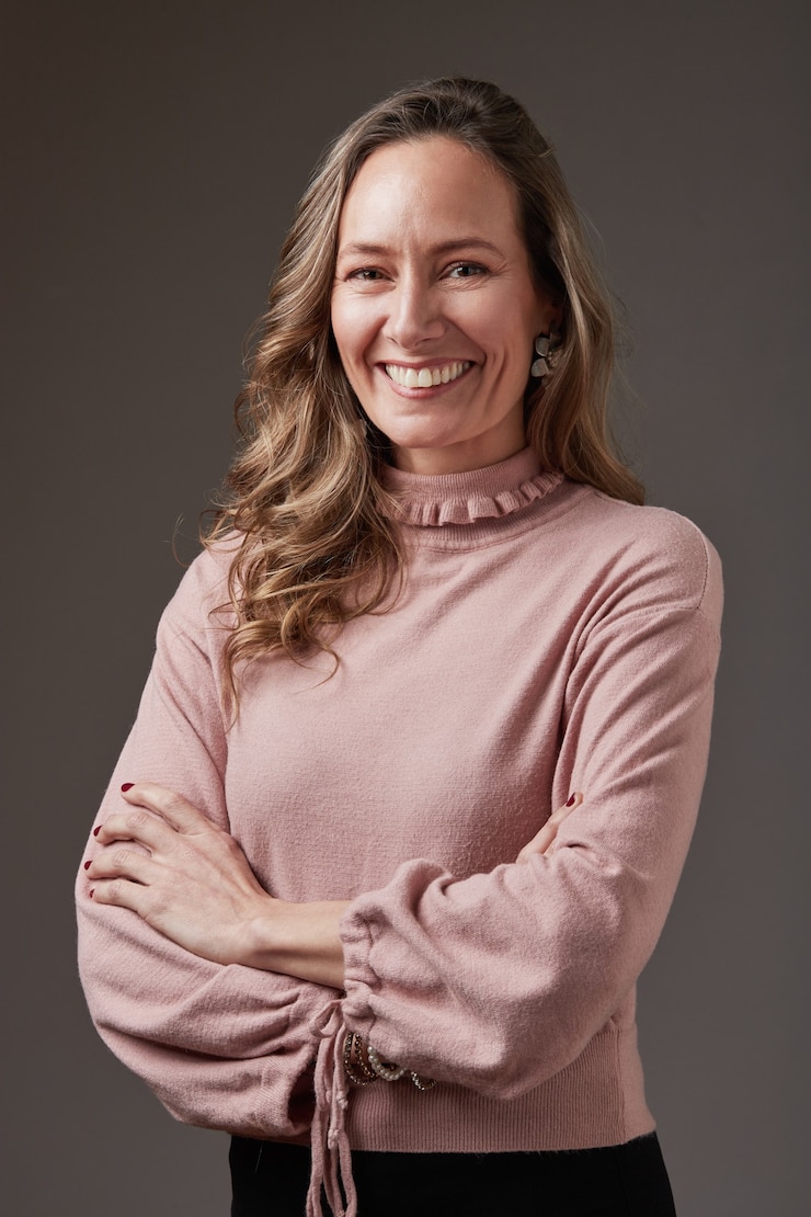 Foto retrato de mujer de negocios rubia sonriente. lleva una blusa celeste sobre un fondo gris. tiene los brazos cruzados