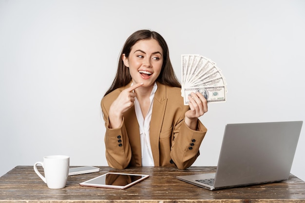 Retrato de mujer de negocios sentada en la oficina con dinero trabajando y obteniendo ganancias posando feliz...