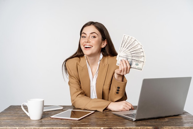 Retrato de mujer de negocios sentada en la oficina con dinero trabajando y obteniendo ganancias posando feliz...