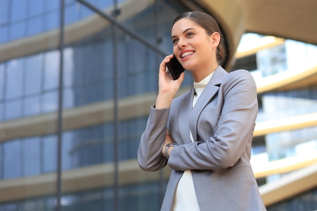 Retrato de mujer de negocios sonriente elegante en ropa de moda llamando por teléfono móvil cerca de la oficina.