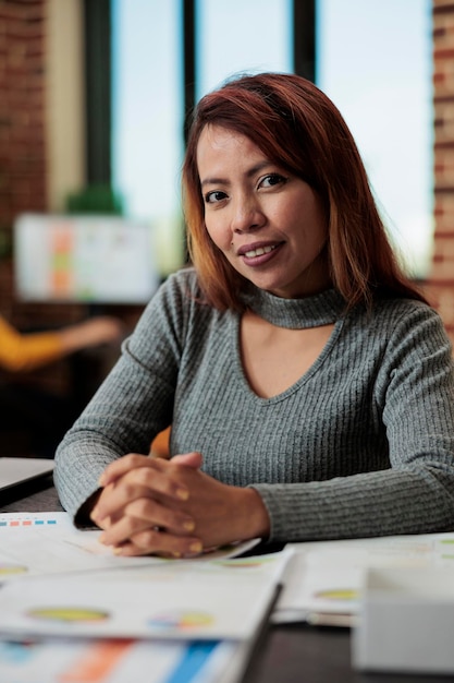 Retrato de una mujer de negocios sonriente que trabaja en un proyecto de marketing analizando los gráficos de la empresa en la oficina de inicio. Gerente ejecutivo sentado en el escritorio lluvia de ideas ideas planificación asociación empresarial