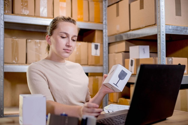 Retrato de una mujer de negocios sosteniendo una caja y escribiendo algo en un teclado mientras prepara la información del paquete Servicio postal y concepto de pequeña empresa