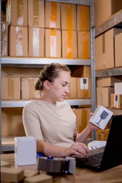 Retrato de una mujer de negocios sosteniendo una caja y escribiendo algo en un teclado mientras prepara la información del paquete Servicio postal y concepto de pequeña empresa