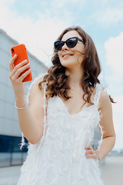 Retrato de una mujer de negocios con un teléfono en las manos contra el fondo de edificios de vidrio Una modelo con un atuendo elegante