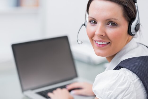 Retrato de mujer de negocios usando auriculares y usando la computadora portátil