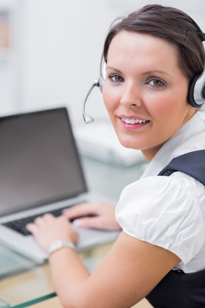 Retrato de mujer de negocios usando auriculares y usando la computadora portátil