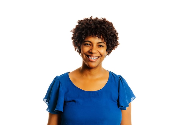 Retrato de una mujer negra con aparatos ortopédicos sonriendo mirando a la cámara sobre un fondo blanco