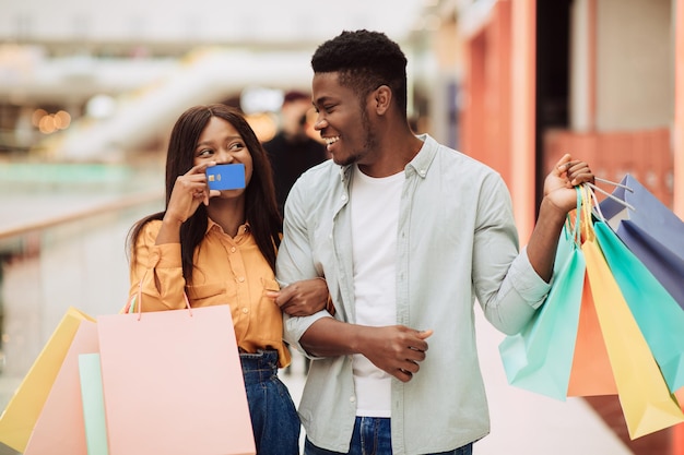 Retrato de mujer negra feliz mostrando tarjeta de crédito al hombre