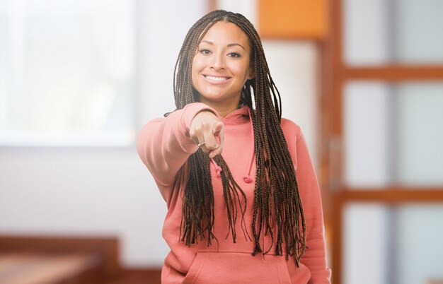 Retrato de una mujer negra joven que llevaba trenzas alegres y sonrientes apuntando al frente