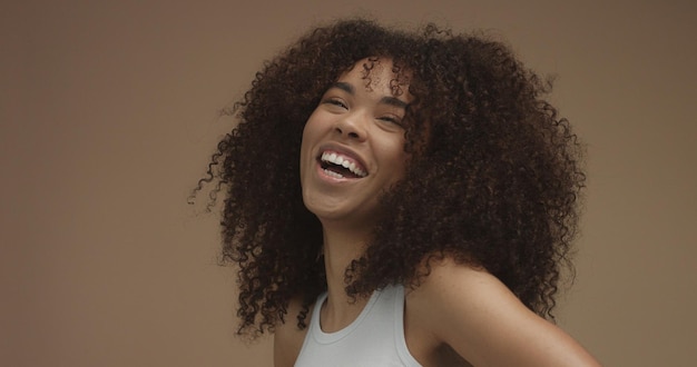 Retrato de mujer negra de raza mixta con pelo rizado de pelo afro grande en fondo beige Risa natural
