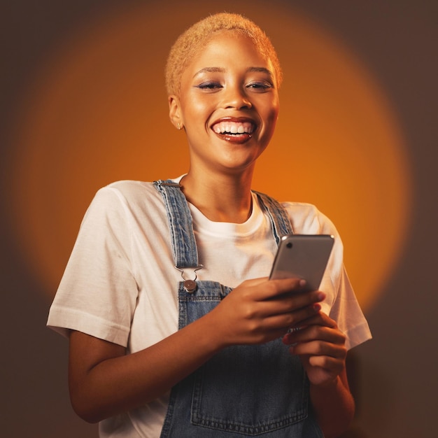 Retrato de una mujer negra sonriendo y escribiendo un mensaje o correo electrónico y navegando por las redes sociales aisladas en el estudio Conexión a Internet y una chica influyente feliz de la moda gen z con un teléfono inteligente en las manos