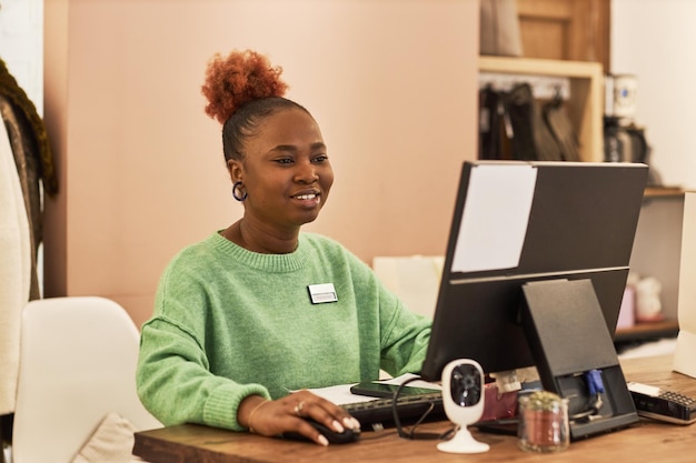Retrato de una mujer negra sonriente usando una computadora mientras trabaja en un espacio de copia de boutique de ropa