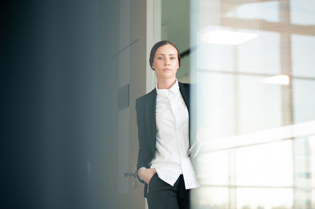 Retrato de mujer de oficina confiada seria en blusa blanca y chaqueta moviéndose sobre el corredor