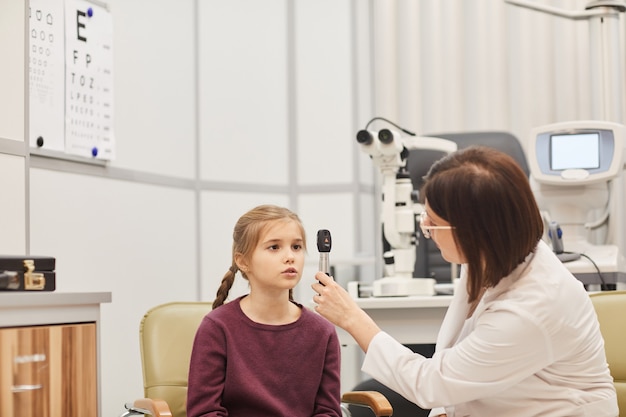 Retrato de mujer optometrista utilizando herramientas mientras comprueba la vista de la niña