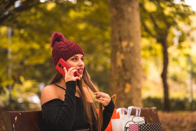 Retrato de una mujer en otoño en un bosque con hojas marrones caminando con bolsas de papel después de ir de compras sentada en el parque