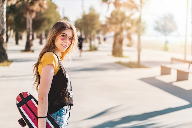 Retrato de una mujer patinadora con gafas rojas y sosteniendo un patín al aire libre