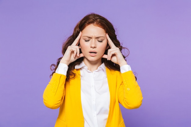 Retrato de una mujer pelirroja joven bastante molesta de pie sobre violeta, con dolor de cabeza