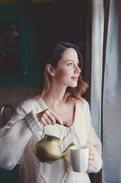 Retrato de mujer pelirroja en suéter y taza de café cerca de la ventana