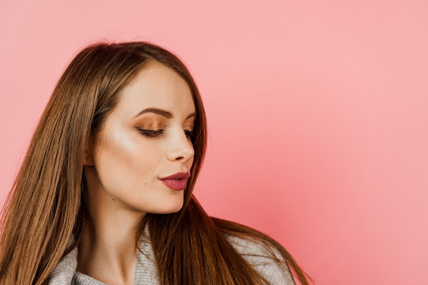 Retrato de una mujer de pelo largo con suéter gris sobre fondo rosa