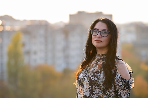 Retrato de una mujer de pelo negro feliz en gafas de moda en un cálido día de verano al aire libre.