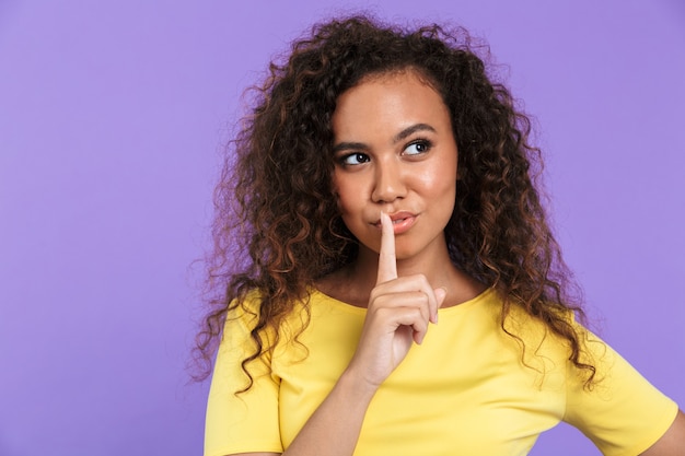 Retrato de mujer de pensamiento afroamericano en ropa casual mostrando gesto de silencio aislado sobre la pared violeta