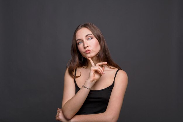 Retrato de mujer pensativa con mirada misteriosa. Chica pensativa toca su barbilla y soñando, fondo oscuro