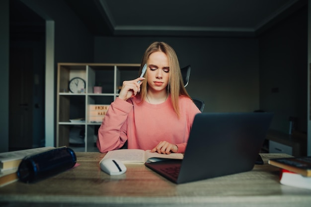 Retrato de una mujer pensativa en un suéter rosa estudiando en casa con una computadora portátil leyendo una tarea